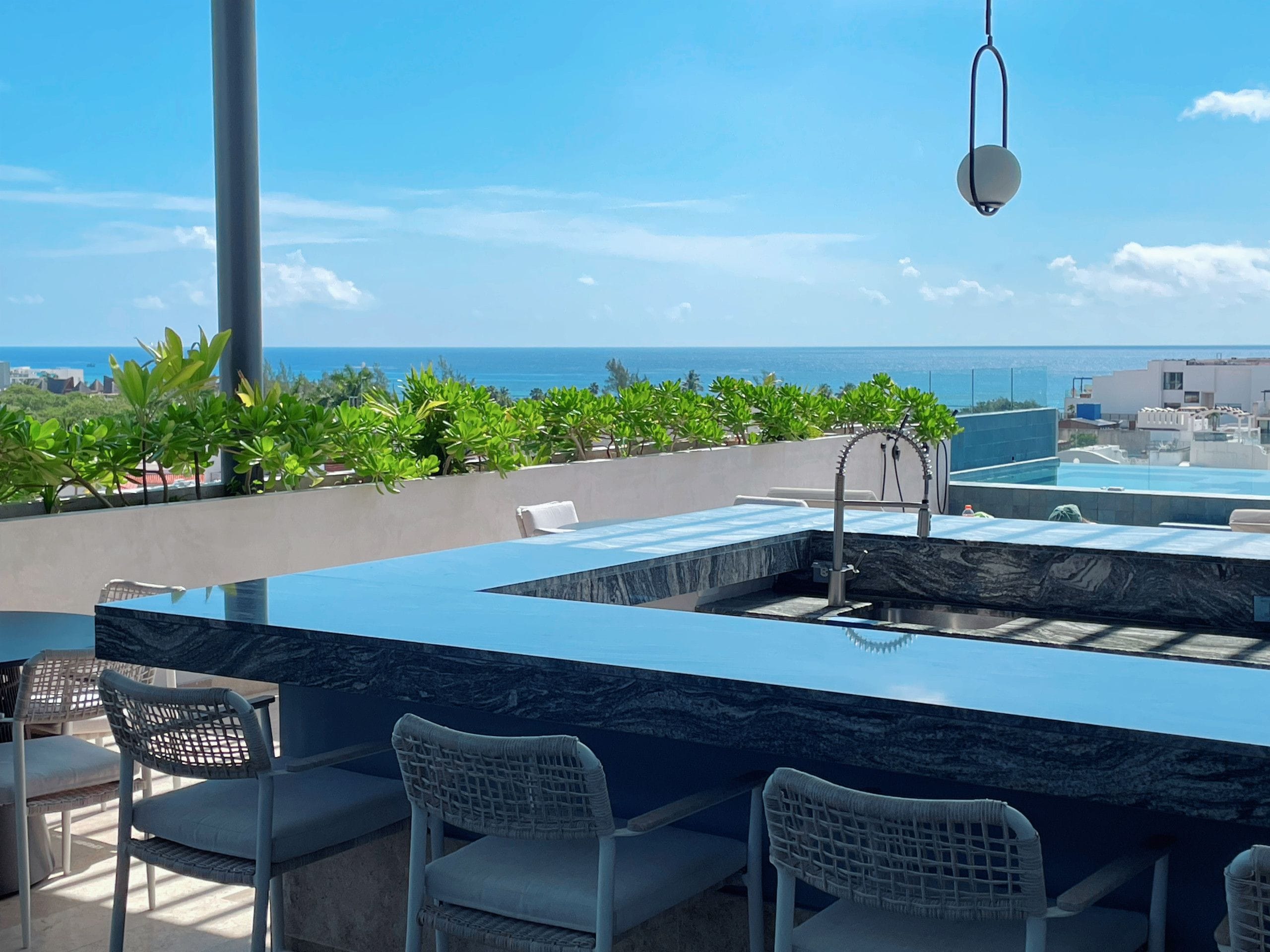 Un bar en la azotea con piscina, mesas al aire libre y vistas al océano.