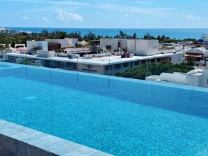 A rooftop pool with clear blue water, surrounded by modern buildings and a view of the ocean. - 5th Ave. Studio Ocean View Rooftop (Playa del Carmen)