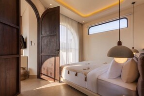 A bedroom with a large bed, a wooden door, a window, and a hanging light fixture. - NEW 3BR Boutique Villa w/ Private Pool - Bingin (South Kuta)