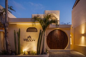 Un bâtiment doté d’une grande porte en bois, d’une enseigne fixée au mur et d’un jardin de cactus.