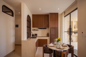 A modern kitchen with wooden cabinets, a built-in oven, and a dining area with a round table set for four. - NEW 3BR Boutique Villa w/ Private Pool - Bingin (South Kuta)