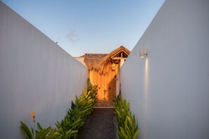 A pathway leading to a building with a thatched roof entrance, flanked by white walls and green plants. - 3BR Garden Villa w/ Expansive Pool in Bingin (South Kuta)
