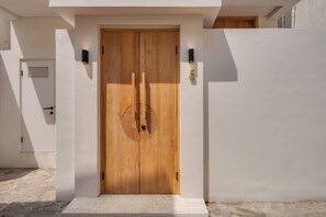 Een houten deur met een rond ontwerp, aan weerszijden omlijst door twee wandlampen, in een modern gebouw met een strak, wit uiterlijk.