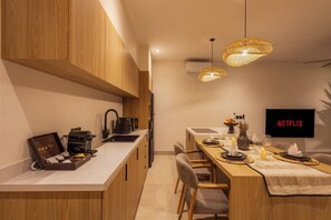 A modern kitchen with wooden cabinets, a built-in coffee machine, and a dining area with a table set for two. - Belluci Uluwatu | 1BR Modern Villa w/ Pvt Pool (South Kuta)
