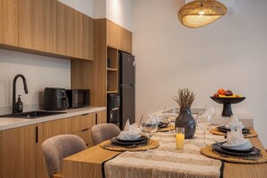 Een moderne keuken met houten kastjes, een zwarte koelkast en een eettafel gedekt voor vier personen, met wijnglazen en een schaal fruit.