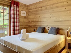 A wooden-paneled room with a bed, pillows, and a window with curtains. - Mont Azur 3 by Interhome (Villars)