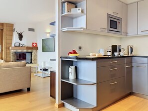 A modern kitchen with built-in appliances, a dining area with a sofa, and a fireplace. - Mont Azur 3 by Interhome (Villars)