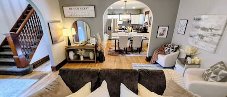A living room with a sofa, a dining area, and a kitchen visible through an archway.