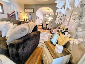 Ein gemütliches Wohnzimmer mit einem dunkelbraunen Sofa, einer weißen Vase mit getrockneten Pflanzen und einem Essbereich im Hintergrund.