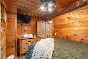 Ein Holzblockhaus-Interieur mit einem Bett, einer Kommode, einem Fernseher und einer Tür.