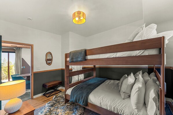 A bunk bed with a wooden frame and white bedding, a bedside table with a lamp, and a mirror on the wall. - Modern Private 3 Acres w/ Hot Tub and Game Room (Bailey)