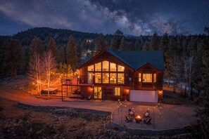 A two-story log cabin with large windows, a deck, and a hot tub. - Modern Private 3 Acres w/ Hot Tub and Game Room (Bailey)
