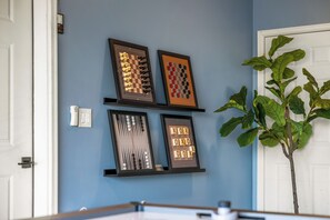 A room with a blue wall, a white door, and a plant. There are four framed chessboards on the wall. - Modern Private 3 Acres w/ Hot Tub and Game Room (Bailey)
