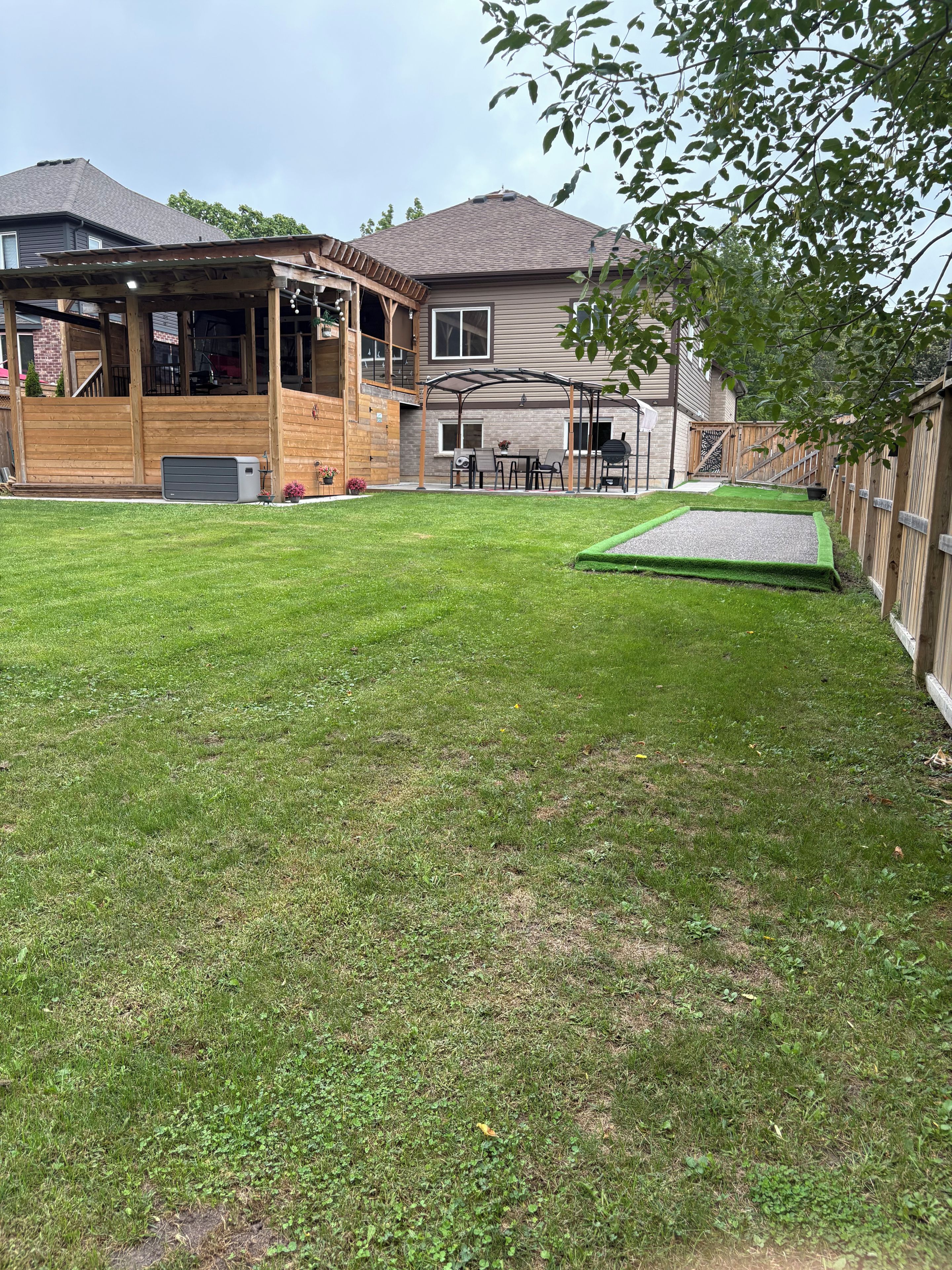 A residential backyard with a wooden deck, a patio area, and a small trampoline.