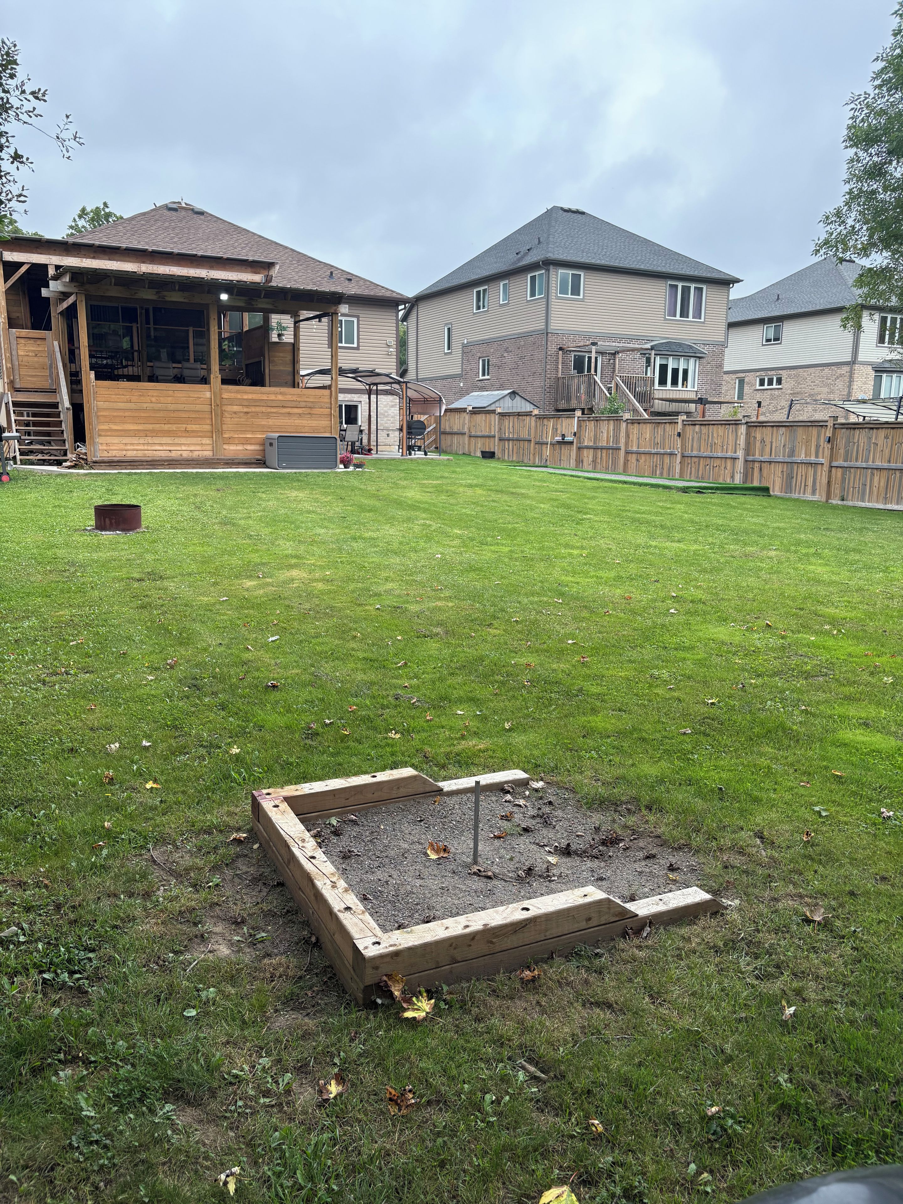A residential backyard with a wooden deck, a raised garden bed, and a fenced area.