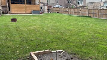 A residential backyard with a wooden deck, a raised garden bed, and a fenced area.