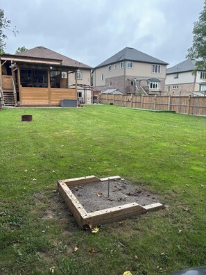 A residential backyard with a wooden deck, a raised garden bed, and a fenced area.
