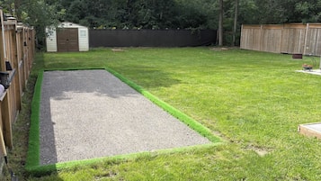 A backyard with a lawn, a gravel area, a wooden fence, and a shed.