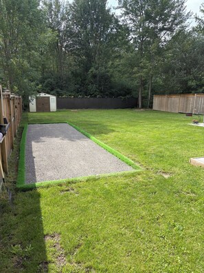 A backyard with a lawn, a gravel area, a wooden fence, and a shed.