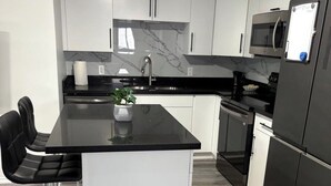 Una cucina moderna con mobili bianchi, un'isola con piano di lavoro nero, elettrodomestici in acciaio inossidabile e una parete di fondo in marmo.