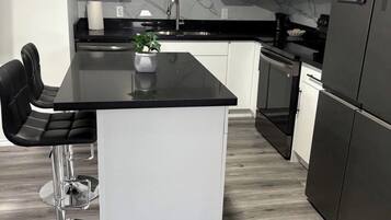 A modern kitchen with white cabinets, a black countertop island, stainless steel appliances, and a marble backsplash.