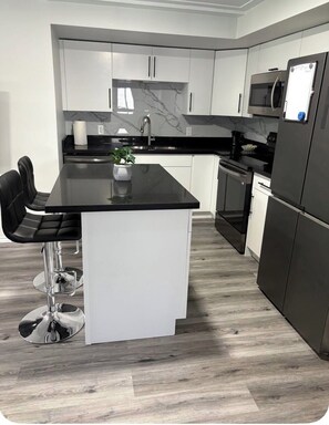 Una cocina moderna con armarios blancos, una isla con encimera negra, electrodomésticos de acero inoxidable y un salpicadero de mármol.