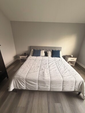 Ein Bett mit weißer, gesteppter Bettdecke, zwei Nachttische mit Lampen und ein Holzboden.