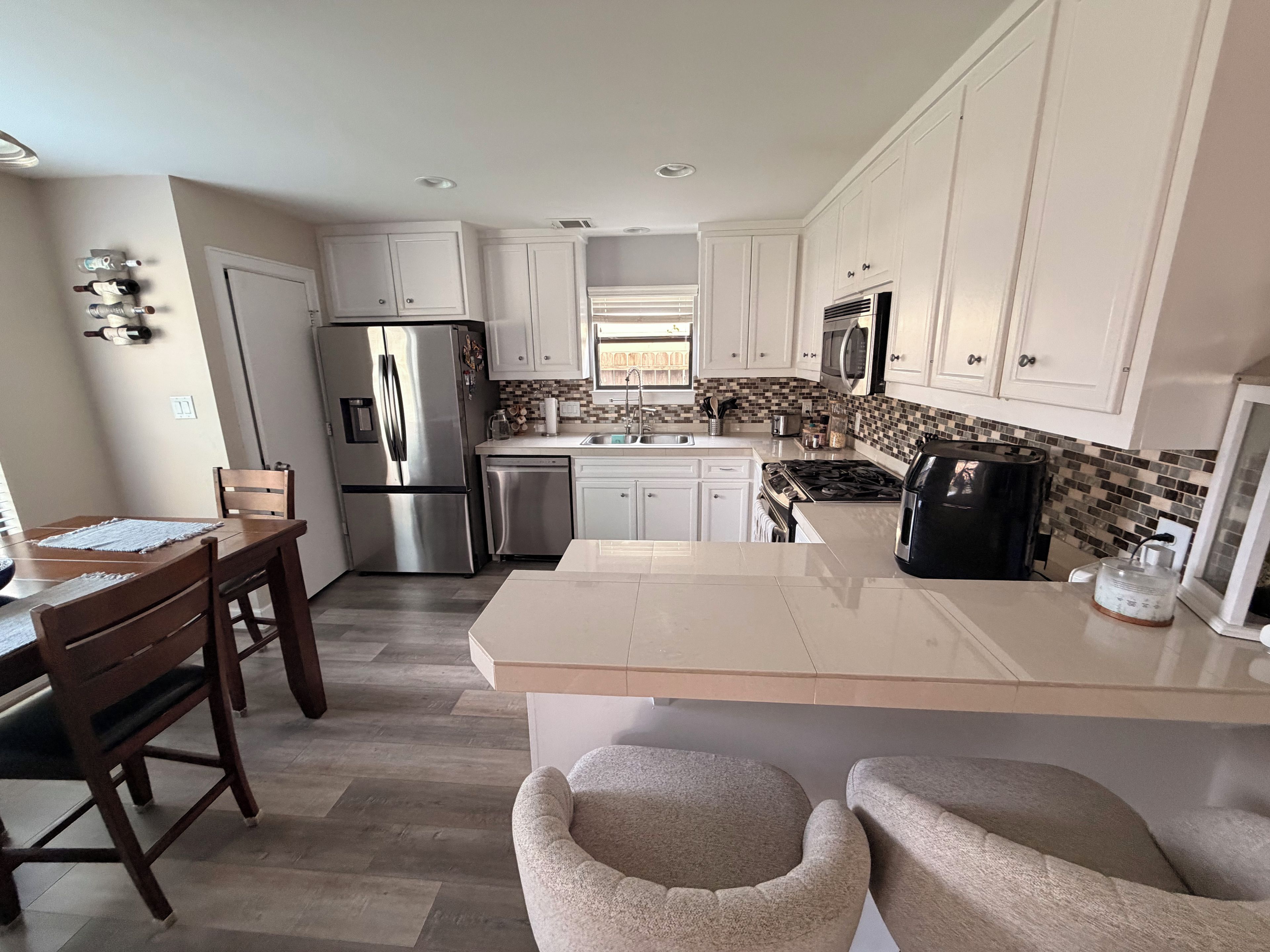 A modern kitchen with white cabinets, stainless steel appliances, a central island, and a dining area with a wooden table and chairs.