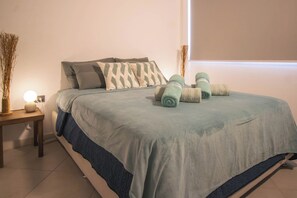 Cama bem arrumada com colcha azul e branca, dois travesseiros e toalhas enroladas sobre a cama.
