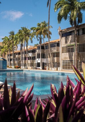 Hotel com piscina, palmeiras e um edifício com varandas.