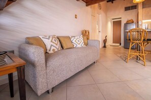 Uma sala de estar acolhedora com um sofá, uma mesa de jantar e uma cadeira de vime.