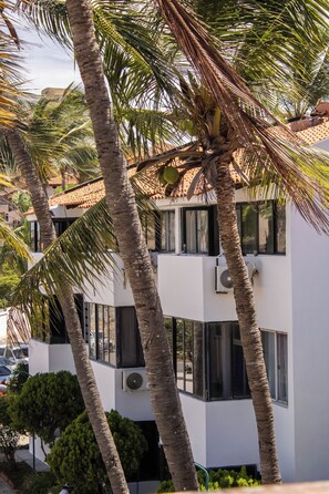 A modern building with multiple balconies, surrounded by palm trees.