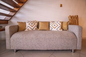A sofa with patterned cushions in a room with a sloped ceiling and a wall-mounted light fixture.