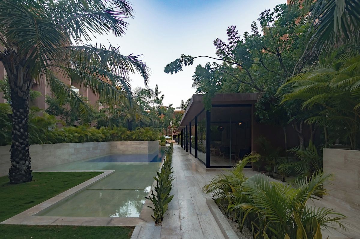 Un espacio exterior moderno con piscina, palmeras y un edificio de cristal.