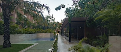 Un espacio exterior moderno con piscina, palmeras y un edificio de cristal.