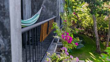 Uma rede pendurada em um corrimão de metal, uma parede de concreto e um jardim com flores cor-de-rosa e folhagem verde.
