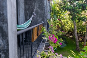 A hammock hanging on a metal railing, a concrete wall, and a garden with pink flowers and green foliage.