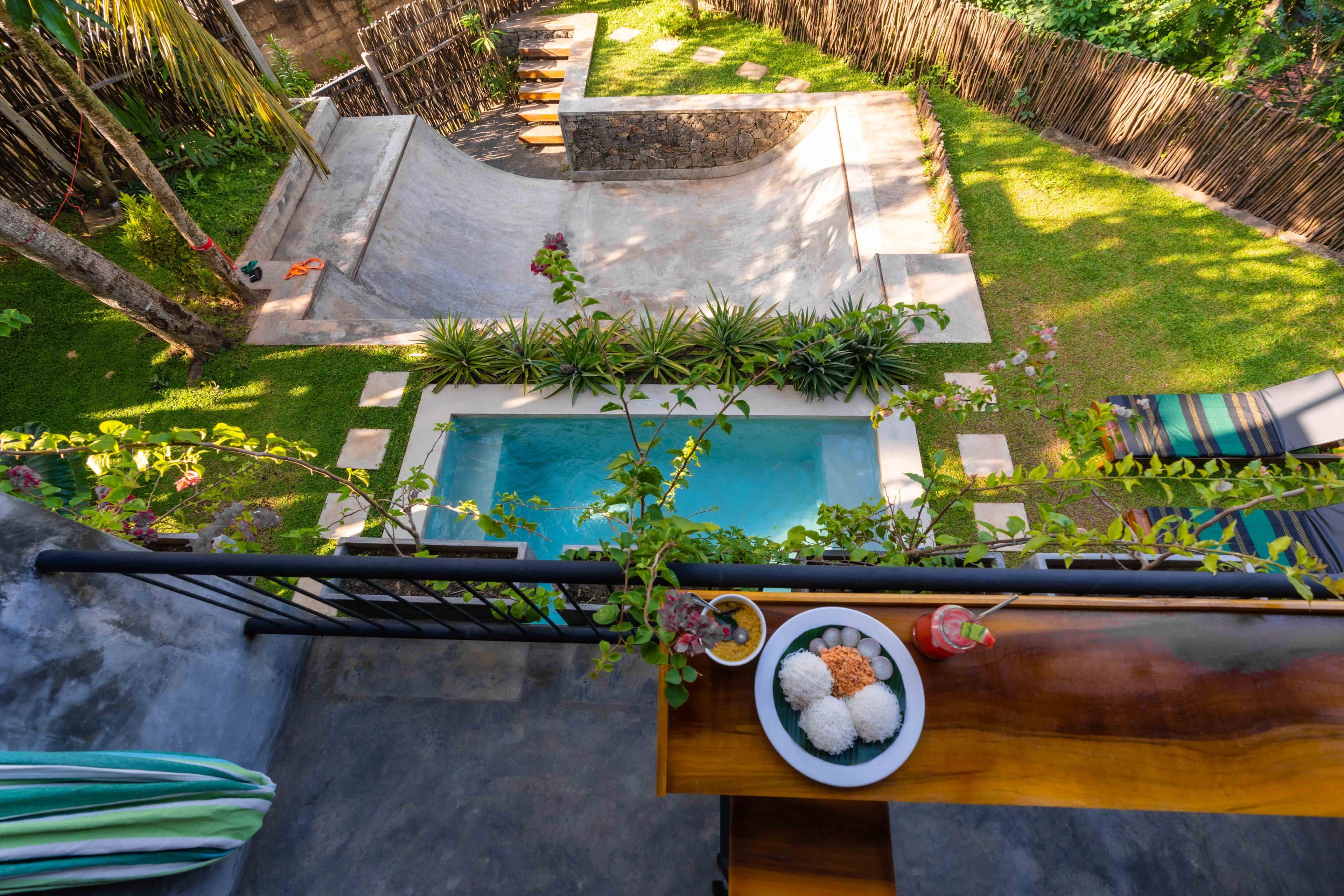 Piscina no terraço com borda de pedra, cercada por vegetação exuberante e cerca de bambu.