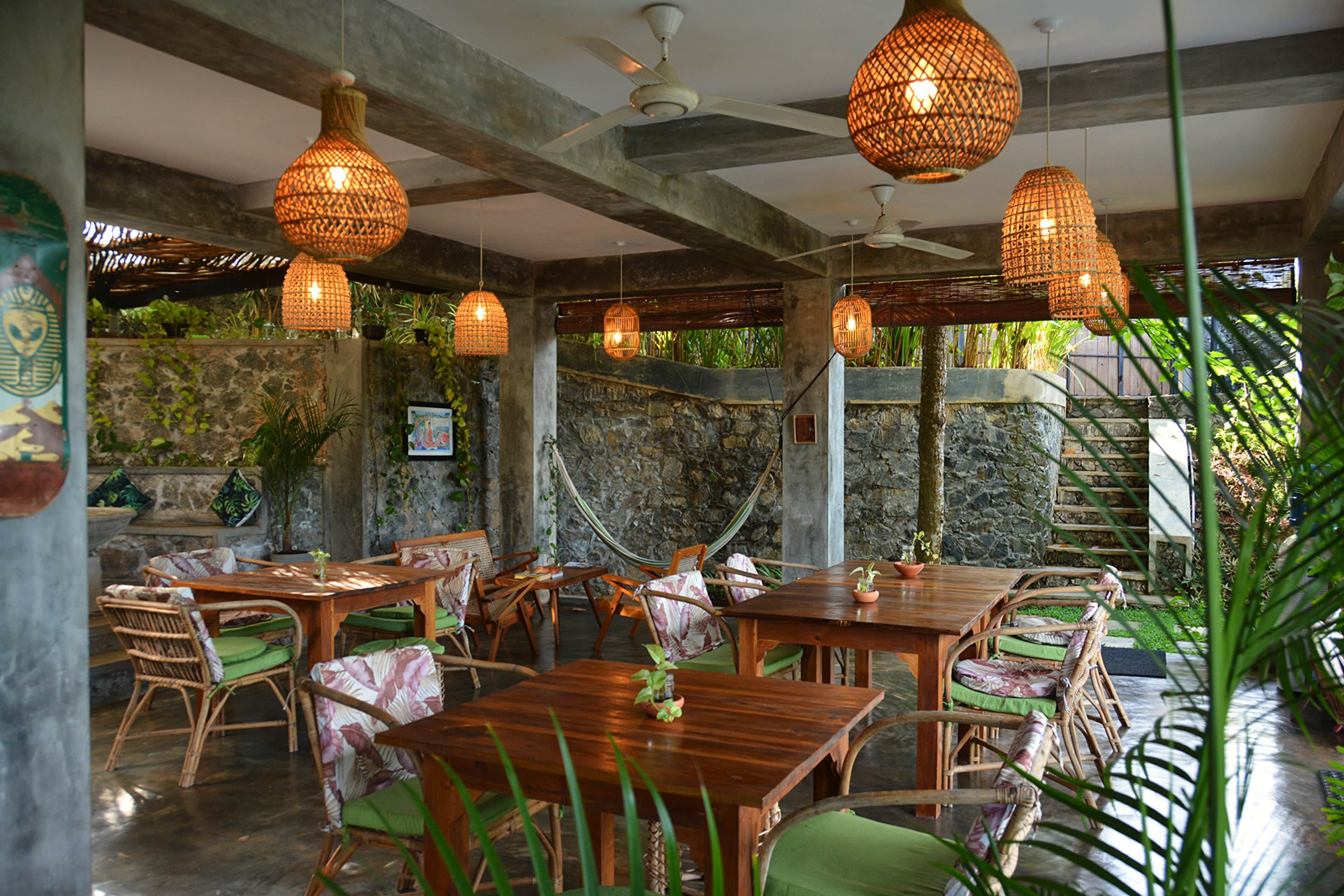 Un espace de restauration intérieur avec des tables et des chaises en bois, des lampes en osier suspendues et un mur en pierre en arrière-plan.