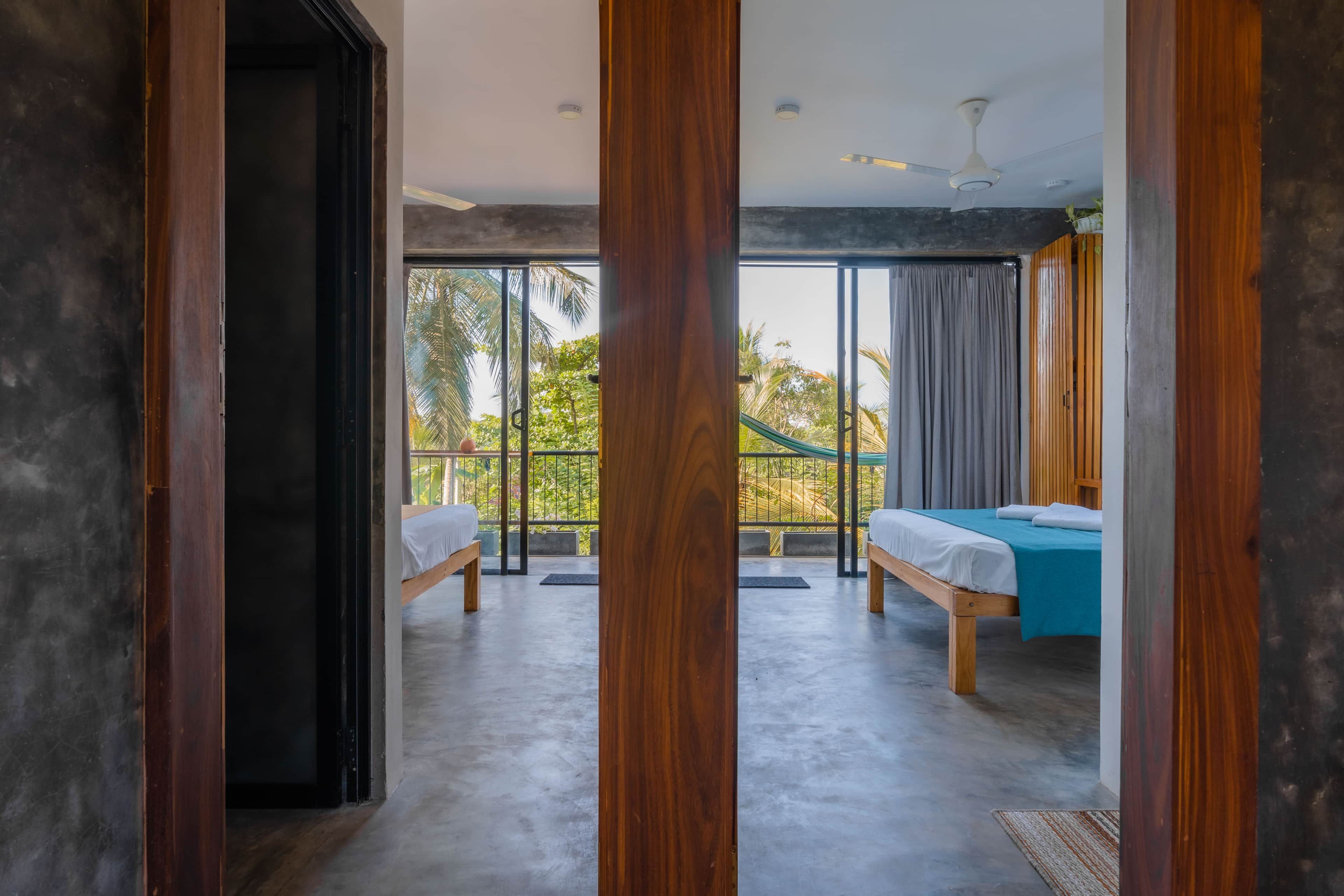 A hotel room with a large sliding glass door leading to a balcony, a bed, a desk, and a ceiling fan.