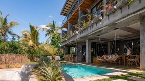 Un edificio moderno con piscina, area salotto esterna e vegetazione lussureggiante.