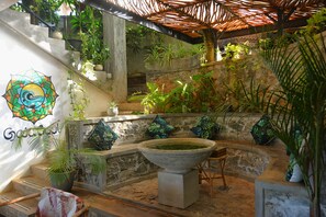 Un escalier en pierre surmonté d’un toit de chaume, entouré d’une végétation luxuriante et de plantes en pot.