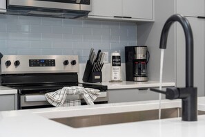 Eine moderne Küche mit einem Edelstahlbackofen, einer Kaffeemaschine und einem Messerblock auf der Arbeitsfläche.