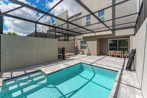 Ein Schwimmbad mit Glasveranda, Gartenmöbeln und blauem Himmel.