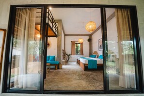 A spacious room with a large sliding glass door leading to an outdoor area, a bed with a blue bedspread, and a staircase. - The Elephant Suite (Maaliyadda)