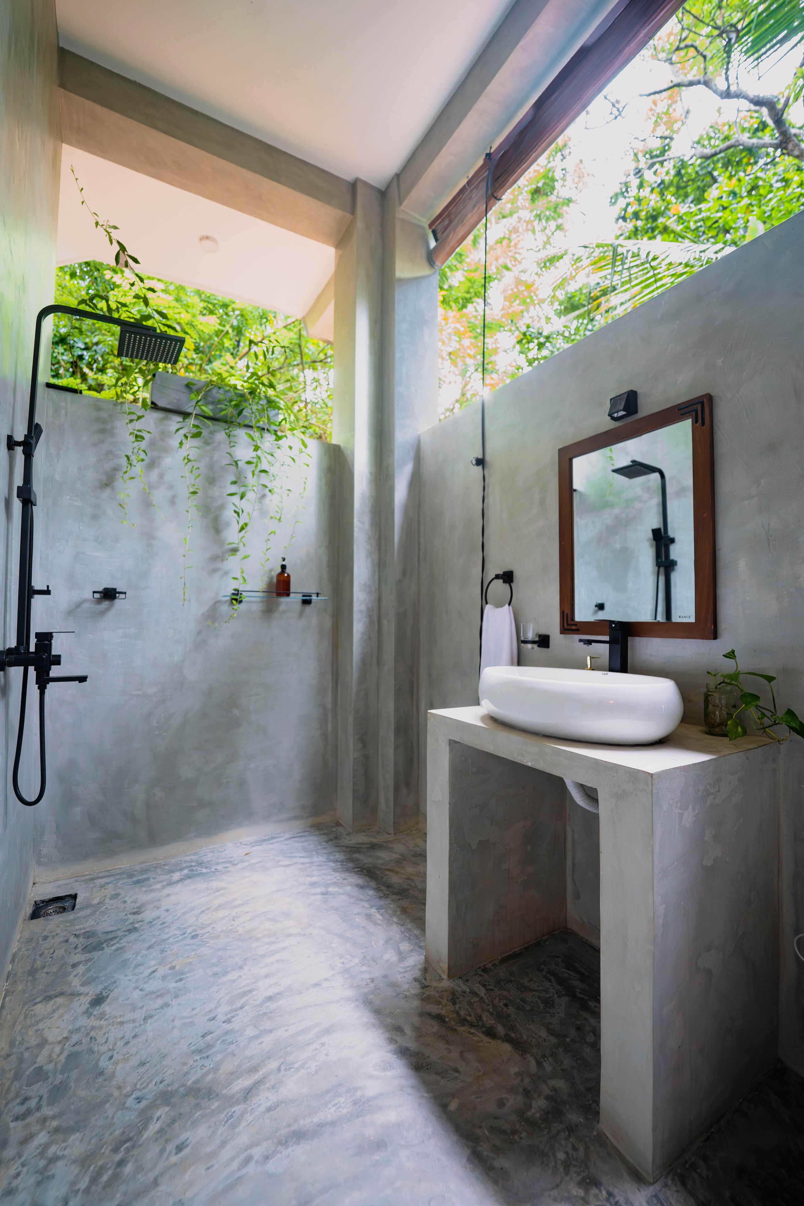 Un baño moderno con un lavabo de concreto, ducha y vista a la vegetación a través del ventanal.