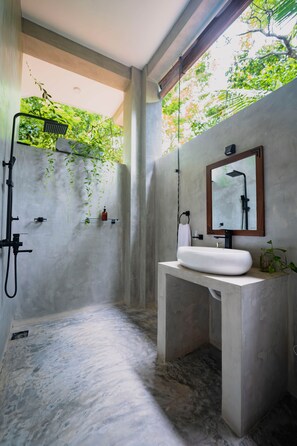 Casa de banho moderna com lavatório de betão, chuveiro e vista para o verde através da janela.