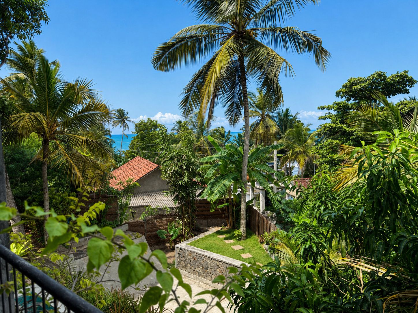 Ein tropischer Garten mit einem Haus, Palmen und blauem Himmel.