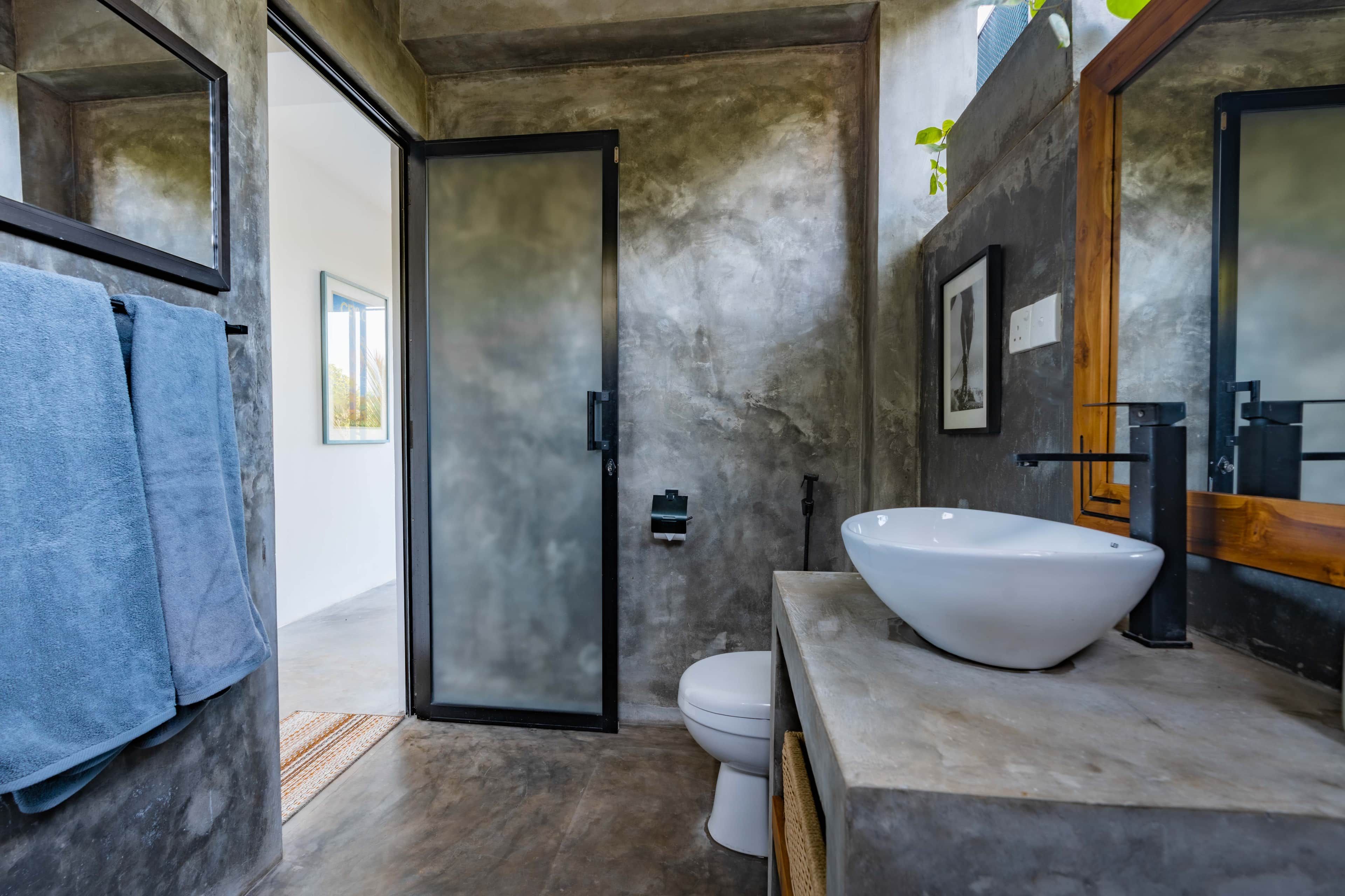 Un baño moderno con un lavamanos grande de color blanco, un inodoro y una puerta que conduce a otra habitación.