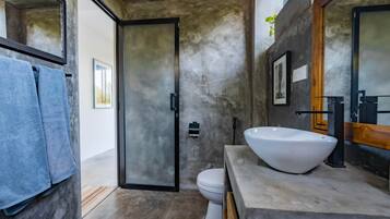 Un baño moderno con un lavamanos grande de color blanco, un inodoro y una puerta que conduce a otra habitación.